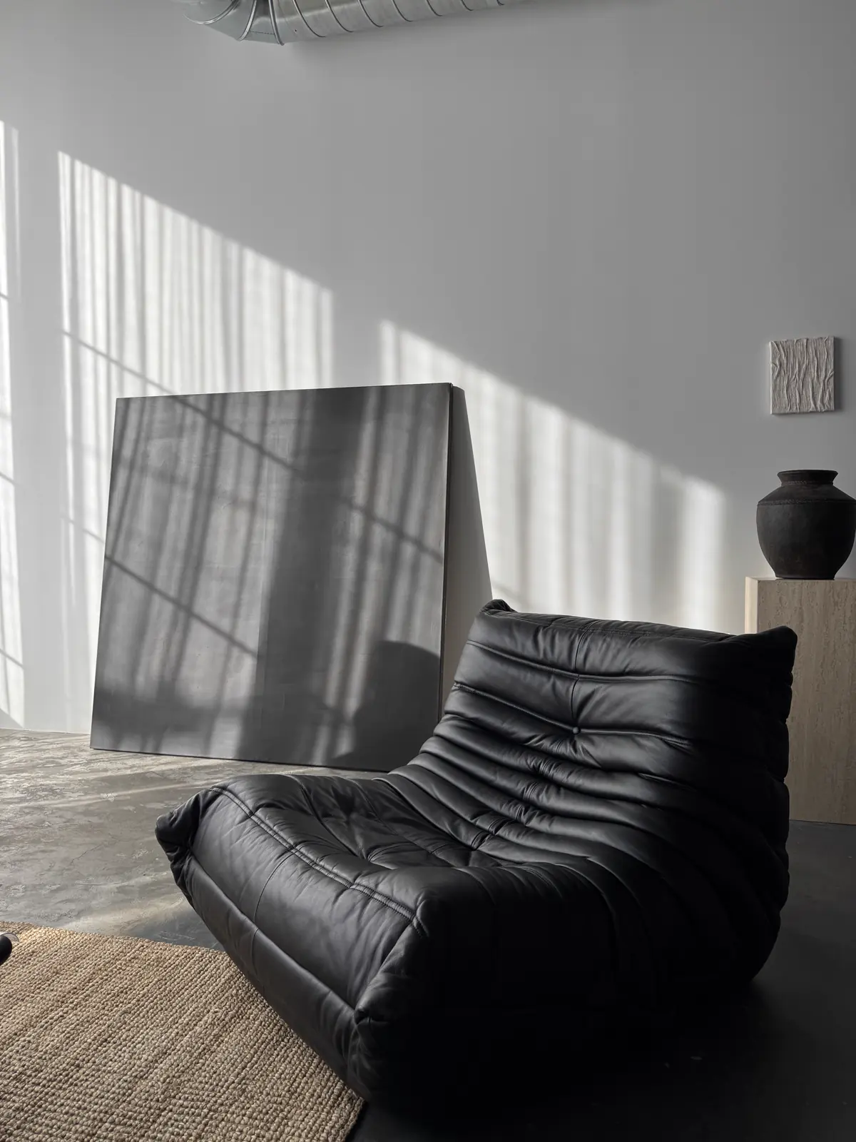 A black leather Togo sofa in raking afternoon light against a pale wall