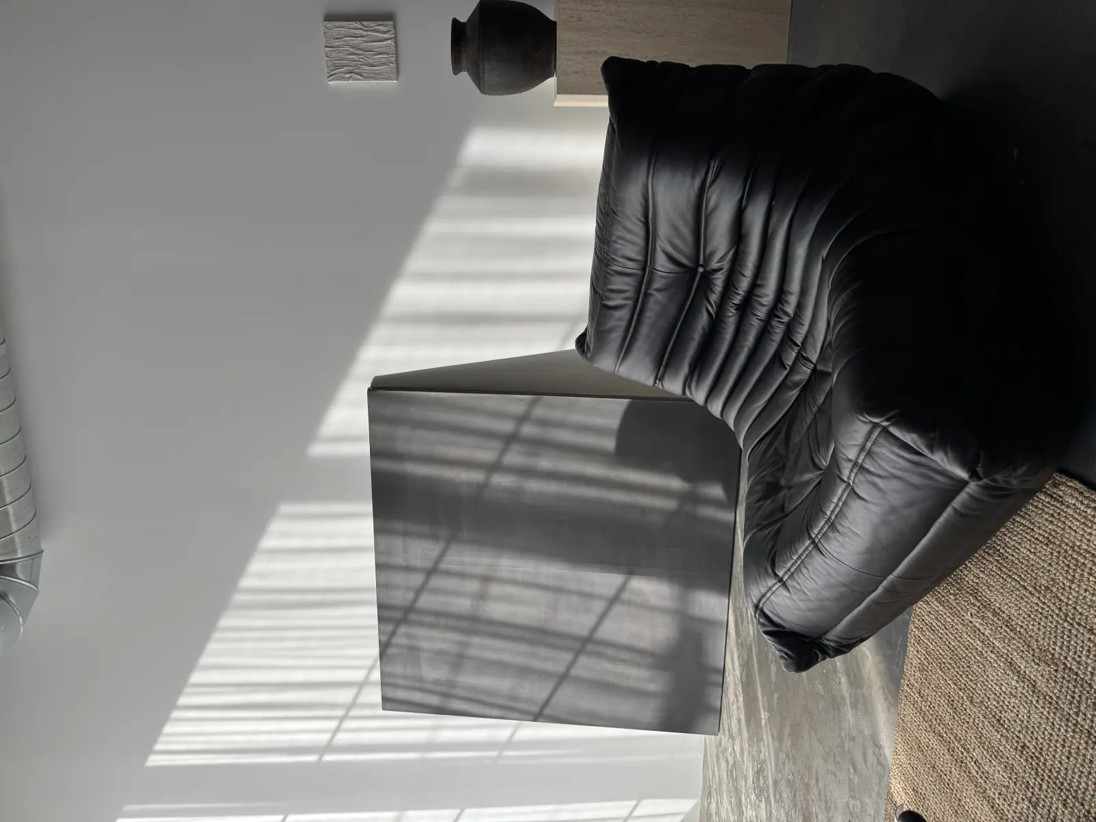 A black leather sofa under hard window light, its shadow thrown across the wall behind