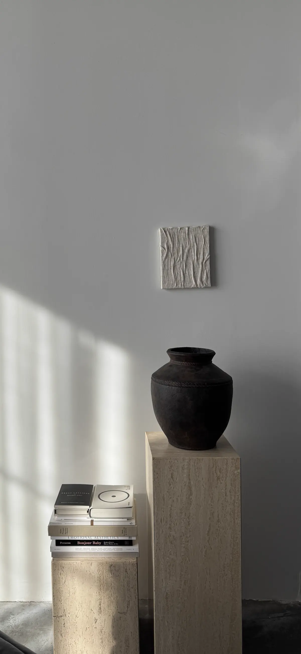 Travertine plinths carrying a dark vase and stacked design books in raking light