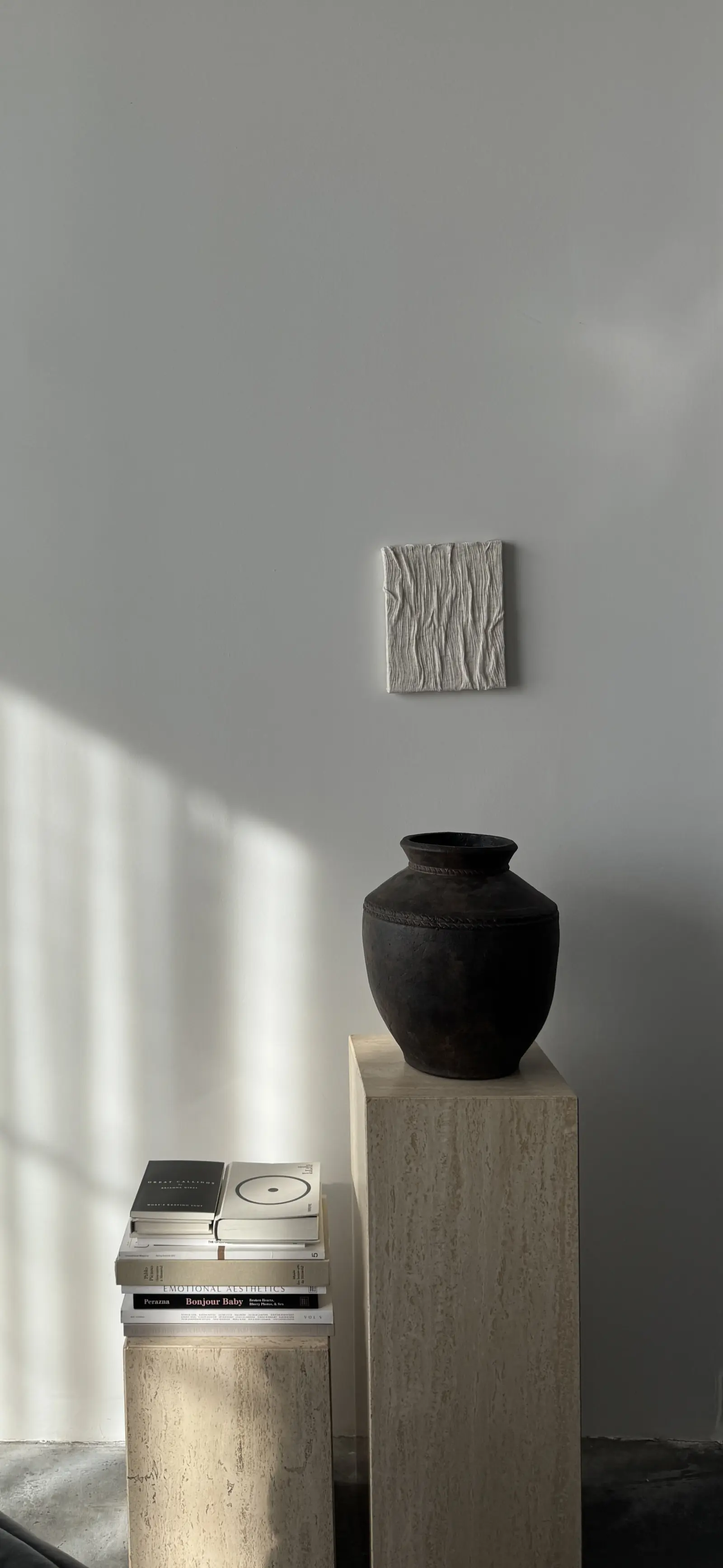 Travertine plinths carrying a dark vase and stacked design books in raking daylight