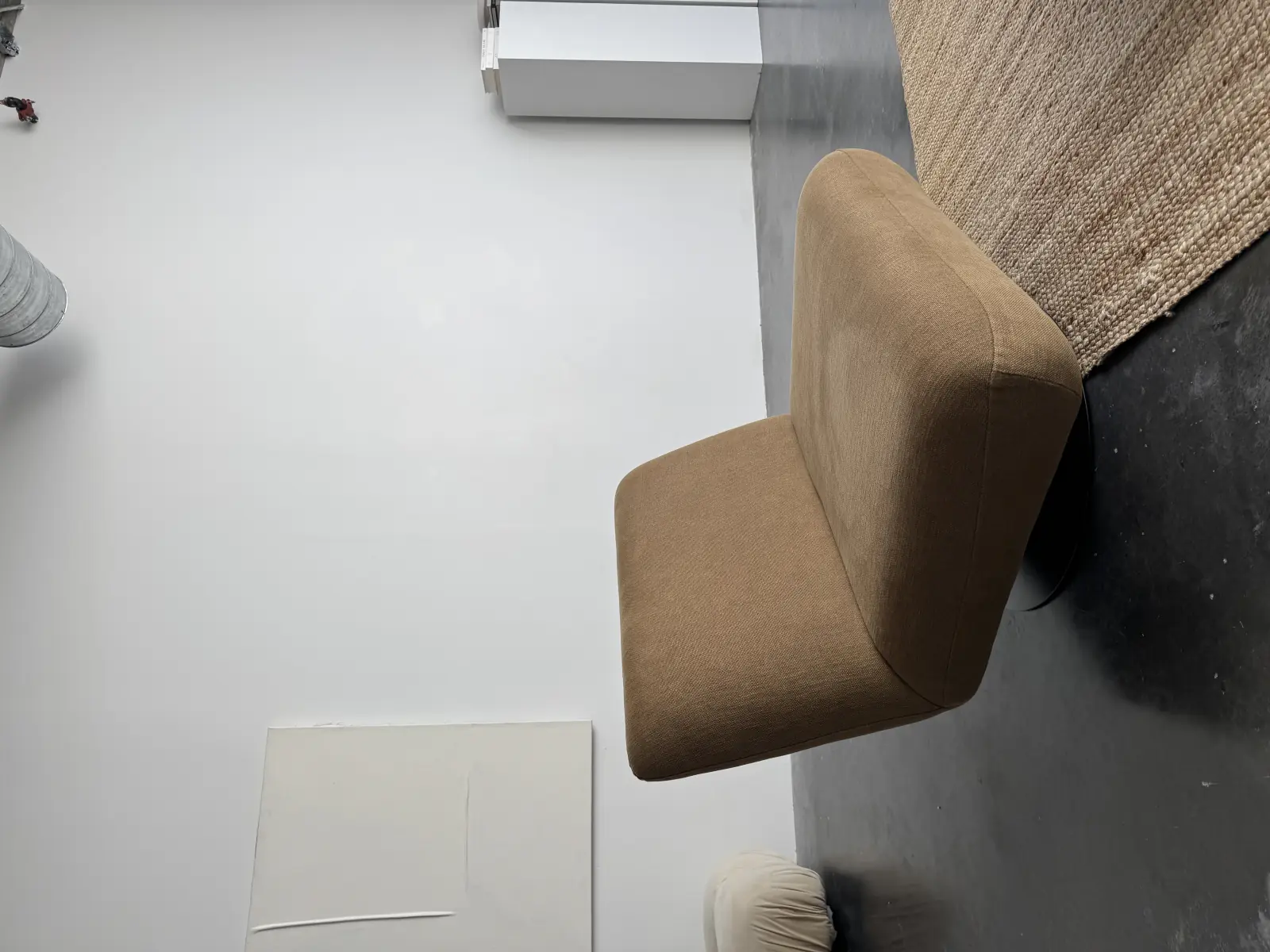 An empty camel-coloured lounge chair on a jute rug in a bare gallery room