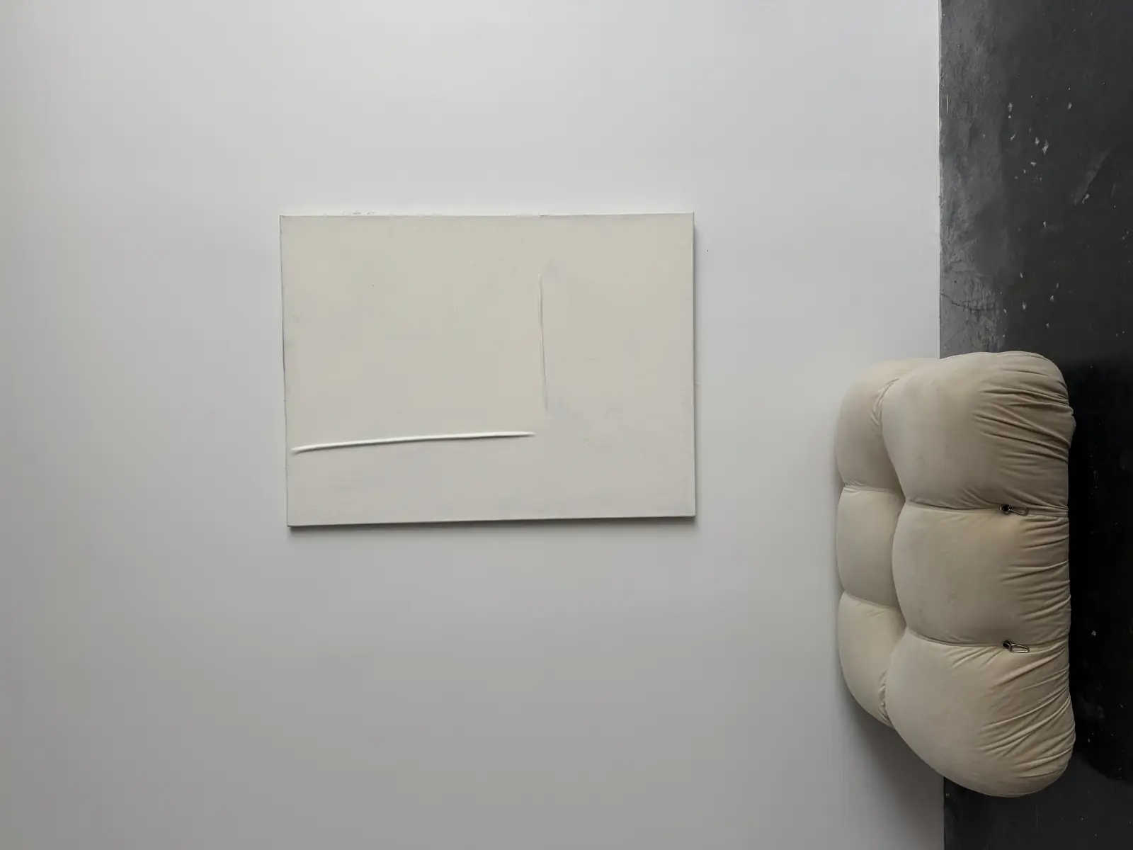 A raw canvas hung above a cream bouclé pouf in a room lit from one side